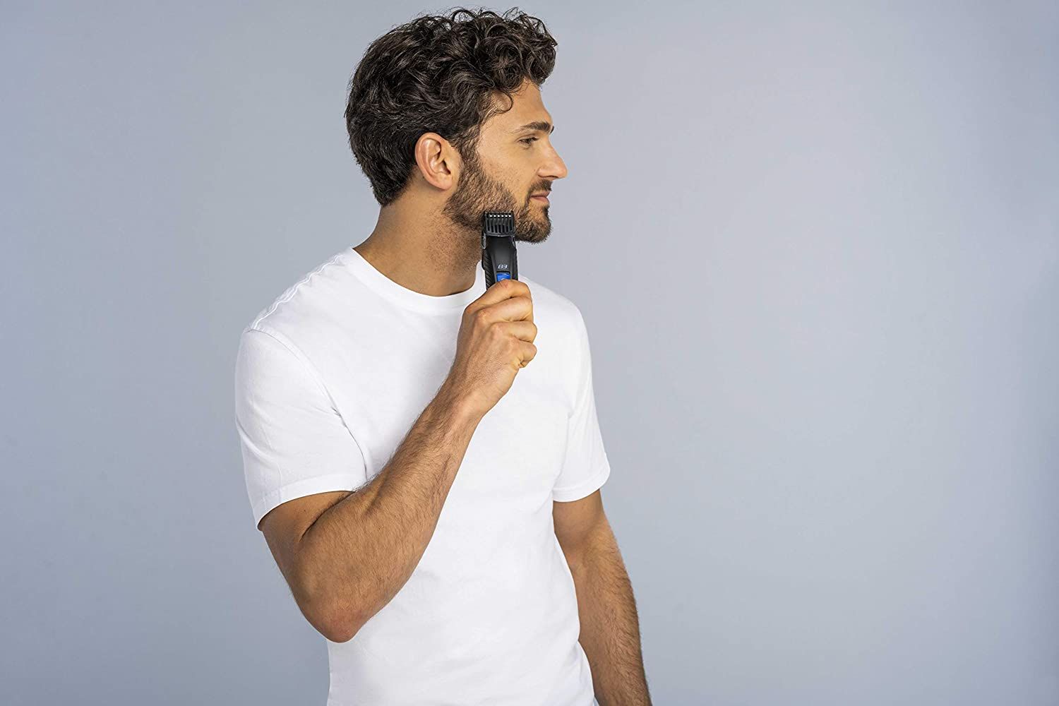 Uomo che si rade con un trimmer nero. Il trimmer è applicato sulla barba dell'uomo. Sfondo grigio.