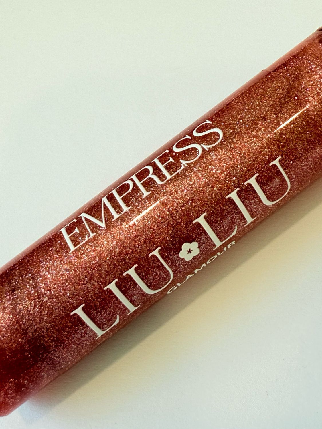 Primo piano del flacone di lucidalabbra. Scritta: EMPRESS LIU LIU Glamour. Lucidalabbra rosso glitterato.