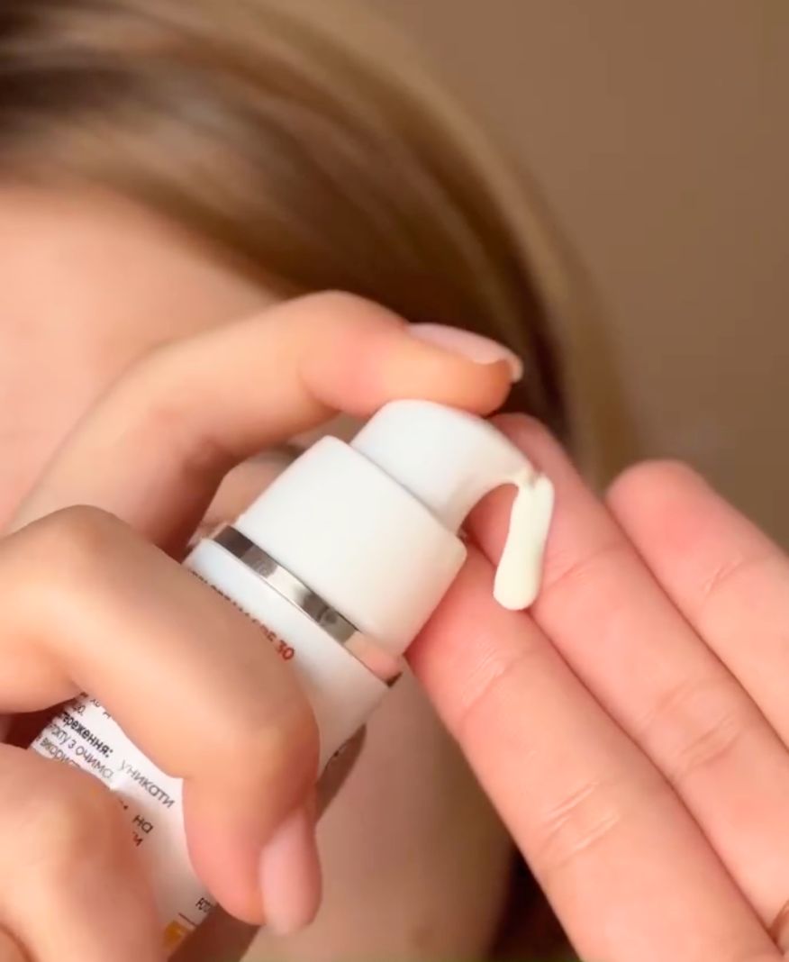 Crema solare erogata da un flacone bianco con dosatore sulla mano.