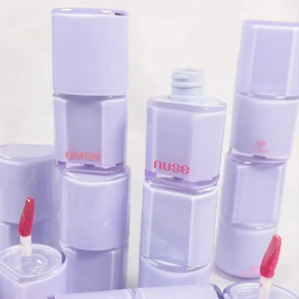 Diversi flaconi di lucidalabbra, viola chiaro con scritta rosa 'nuse'. Alcuni con applicatore.