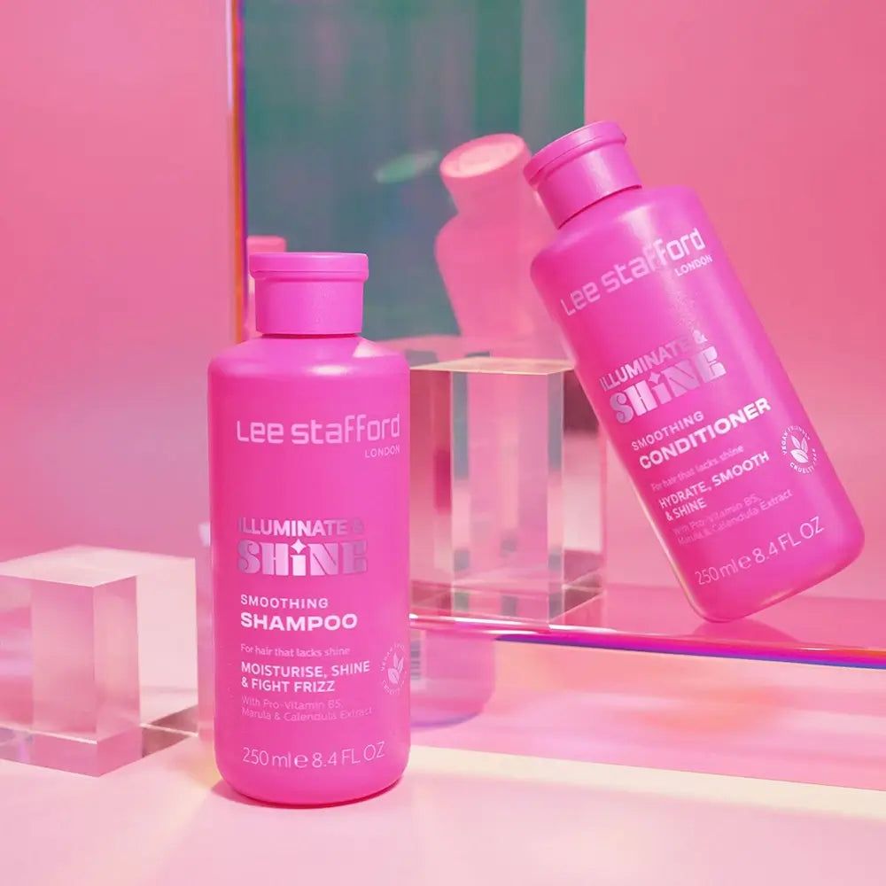 Due bottiglie rosa di prodotti Lee Stafford, un balsamo e uno shampoo, su una superficie di vetro.