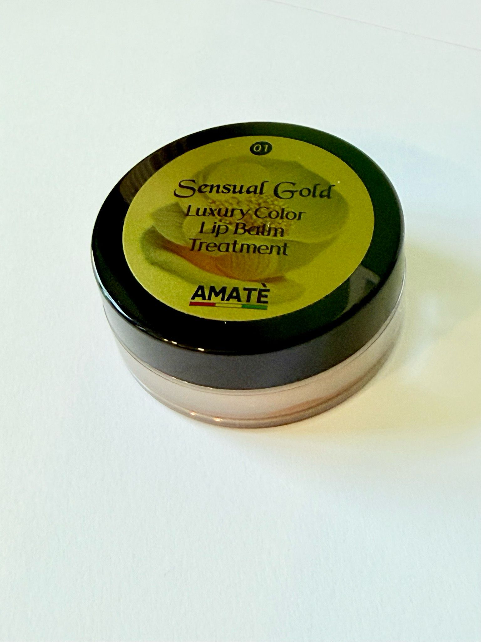 Vasetto rotondo di Sensual Gold Lip Balm Treatment. Coperchio nero, adesivo dorato con informazioni e logo AMATÈ.