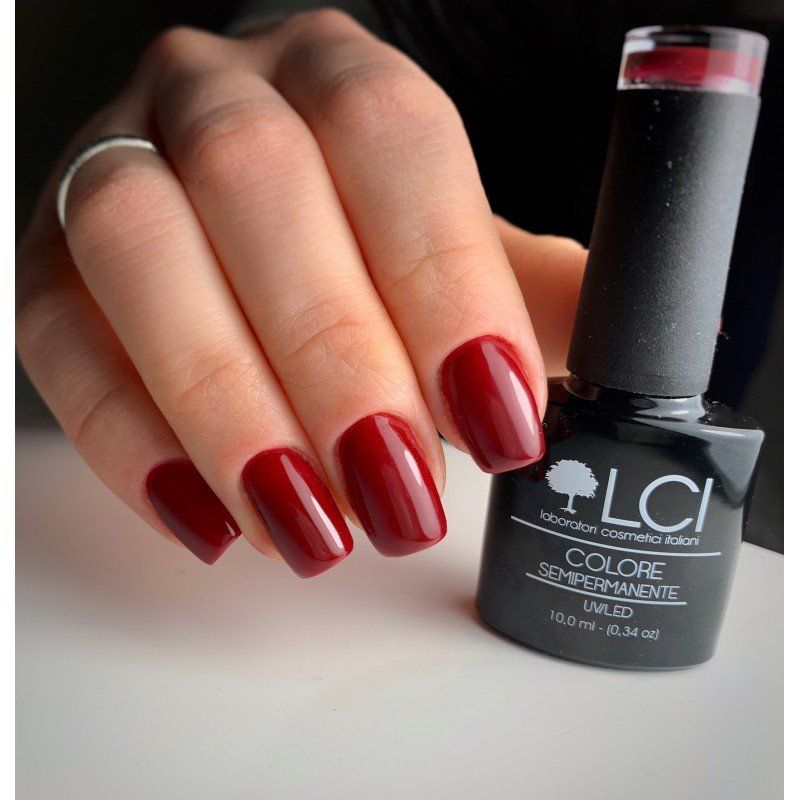 Mano con unghie rosse smaltate e flacone di smalto. Scritta: LCI, COLORE SEMIPERMANENTE, UVLED.