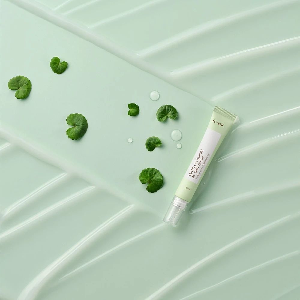 Tubo verde su sfondo verde con foglie e gocce d'acqua. Scritta: iUNIK, Centella Calming AC Spot Cream.