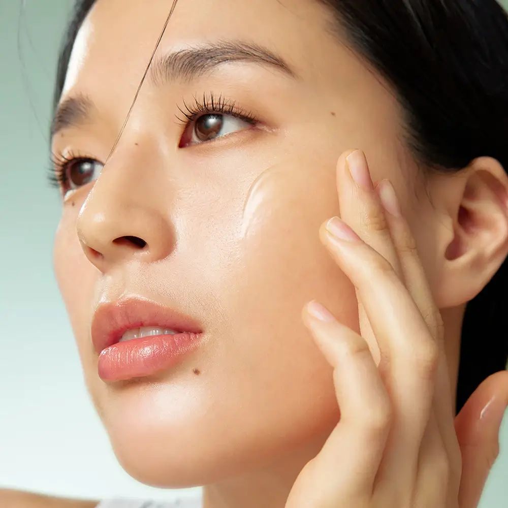 Viso di donna. Applicazione di siero. La pelle brilla. Prodotto non visibile.
