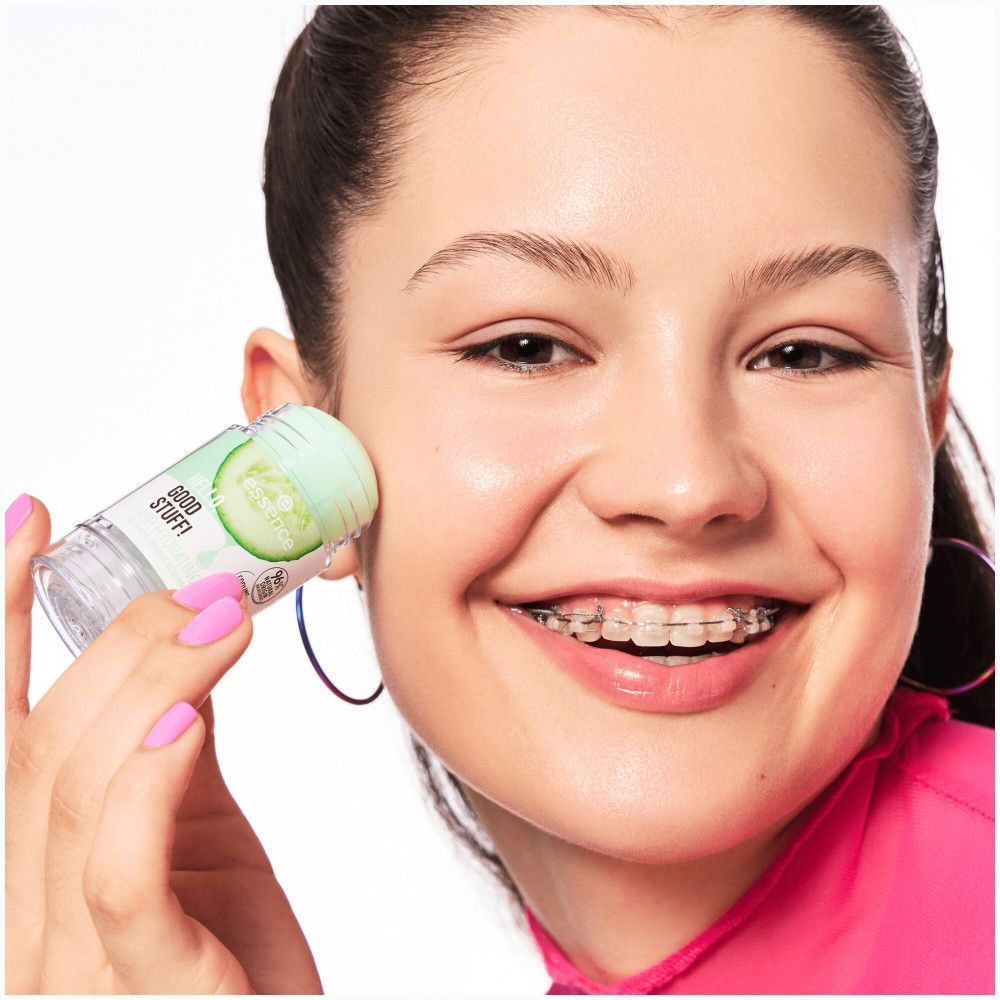 Giovane donna applica stick siero. Prodotto con motivo cetriolo. Unghie smaltate rosa. Viso con apparecchio.