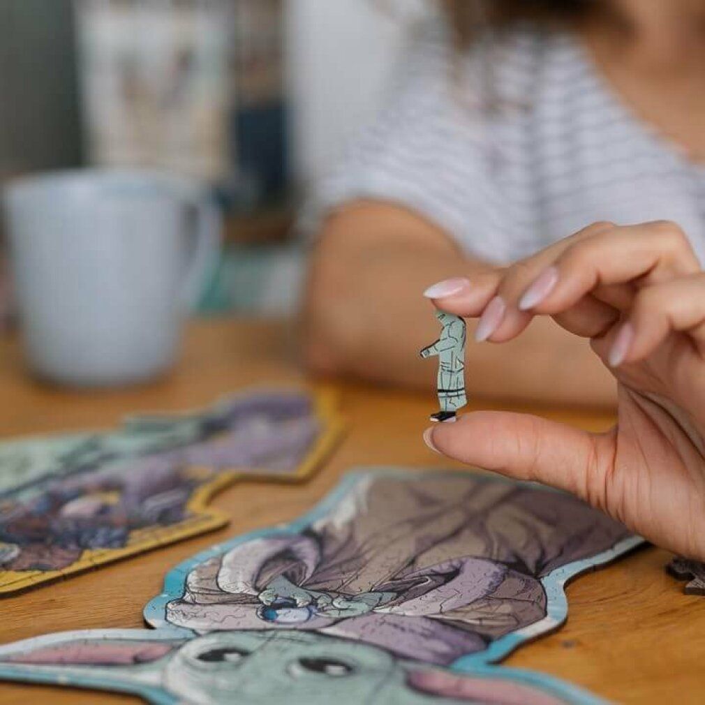 Persona che tiene in mano un piccolo pezzo di puzzle. Parte di un puzzle Grogu. Materiale legno.