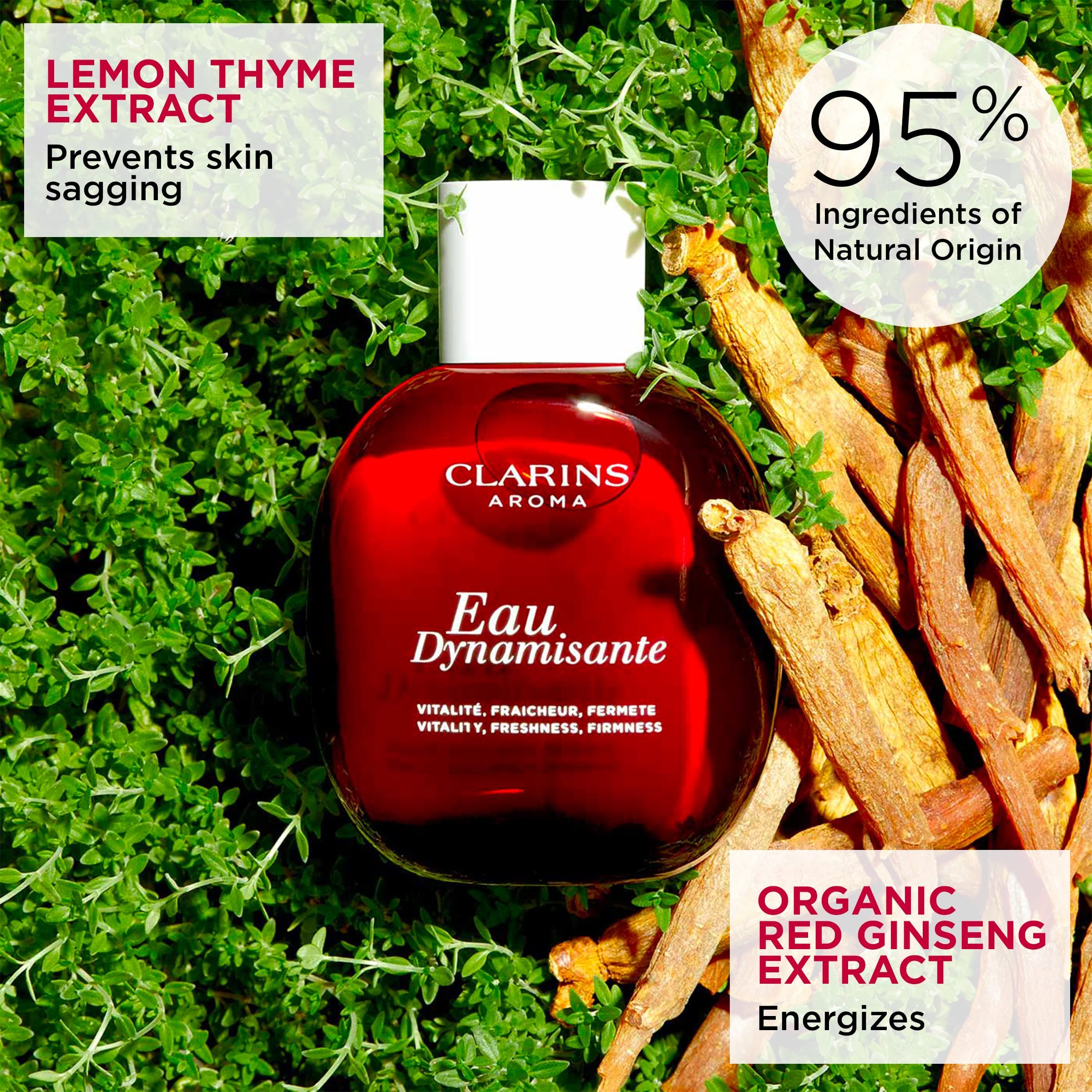 Flacone rosso Clarins Aroma Eau Dynamisante, circondato da erbe e zenzero. Testo: 95% ingredienti di origine naturale.