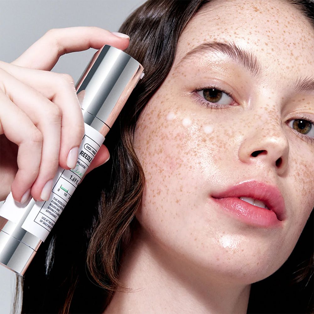Una donna tiene una fiala VT Cosmetics Reedle Shot davanti al viso con l'essenza applicata.