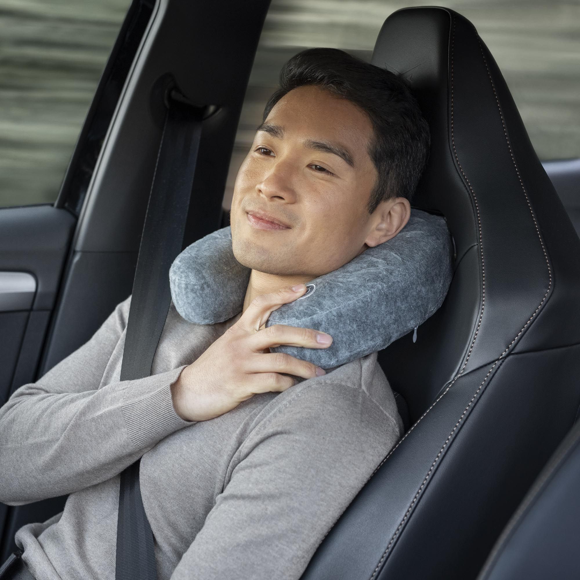 Uomo in auto con cuscino per il collo grigio. Indossa la cintura di sicurezza.