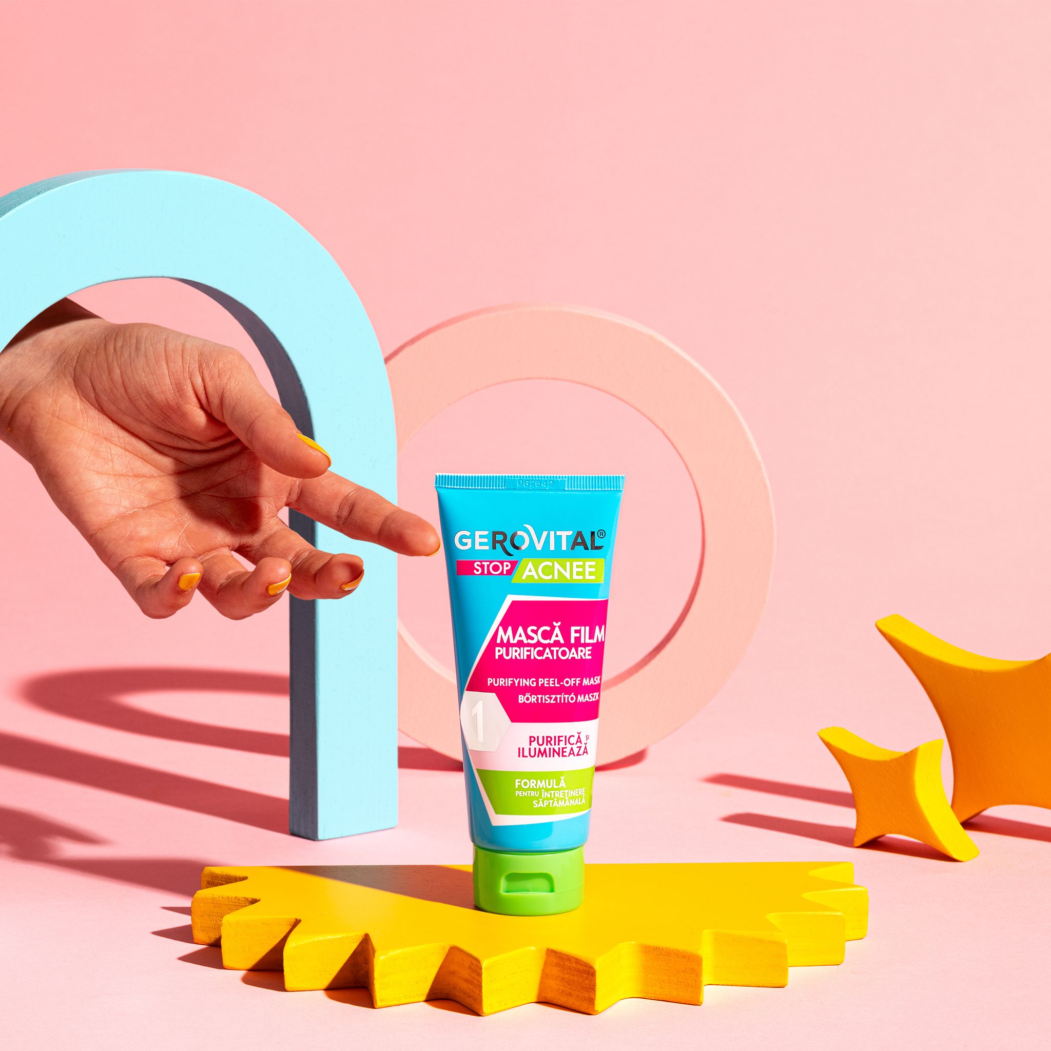Mano che indica un tubo blu-verde. Scritta: Gerovital Stop Acnee, Mască Film Purificatoare, Purifying Peel-off Maske.