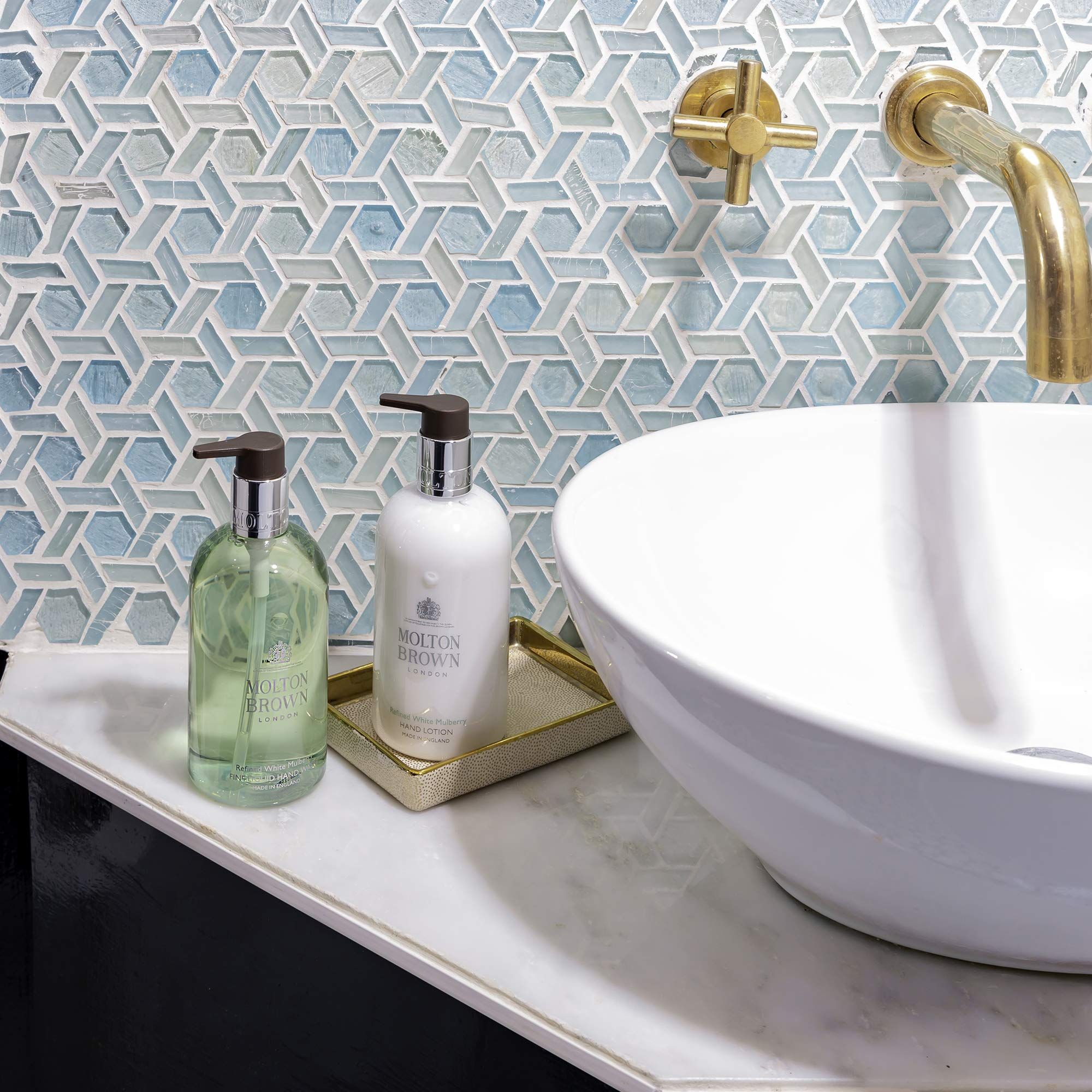 Due flaconi di lozione per le mani vicino a un lavandino. Un flacone verde e uno bianco con dosatore. Scritta: Molton Brown.