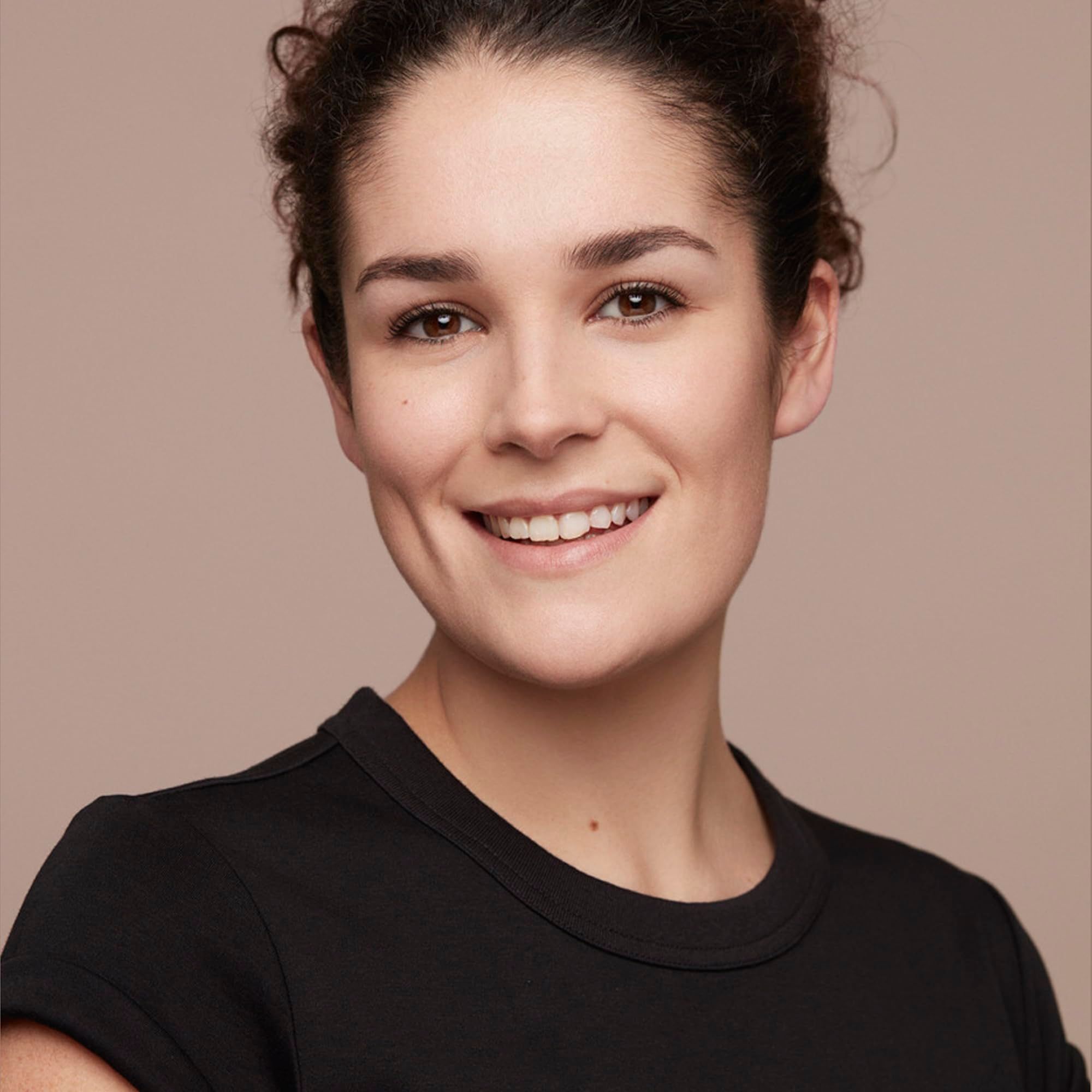 Ritratto di donna sorridente con capelli scuri, indossa una maglietta nera. Sfondo marrone chiaro.