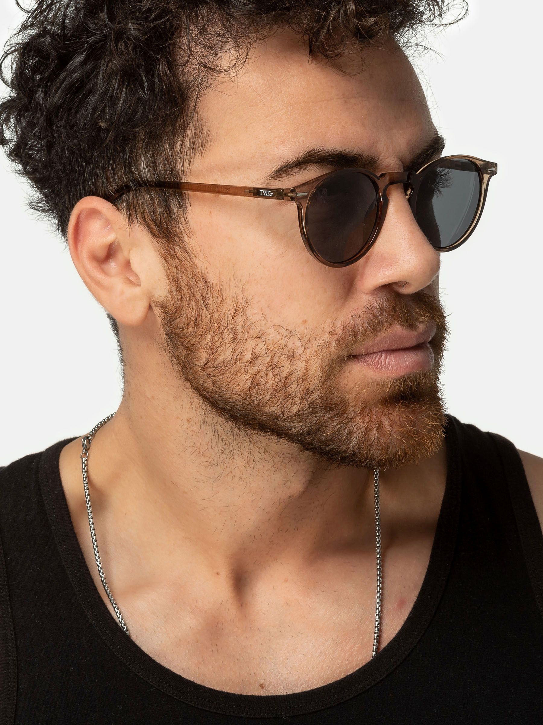 Uomo con occhiali da sole Twig. Montatura rotonda marrone, lenti scure.