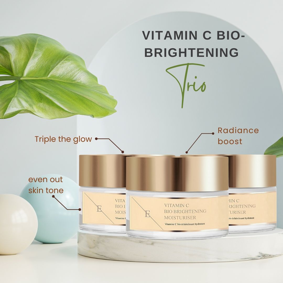 Tre vasetti con coperchi dorati. Le etichette riportano: Vitamin C Bio Brightening Moisturiser. Testo: Trio, Radiance boost, even out skin tone.