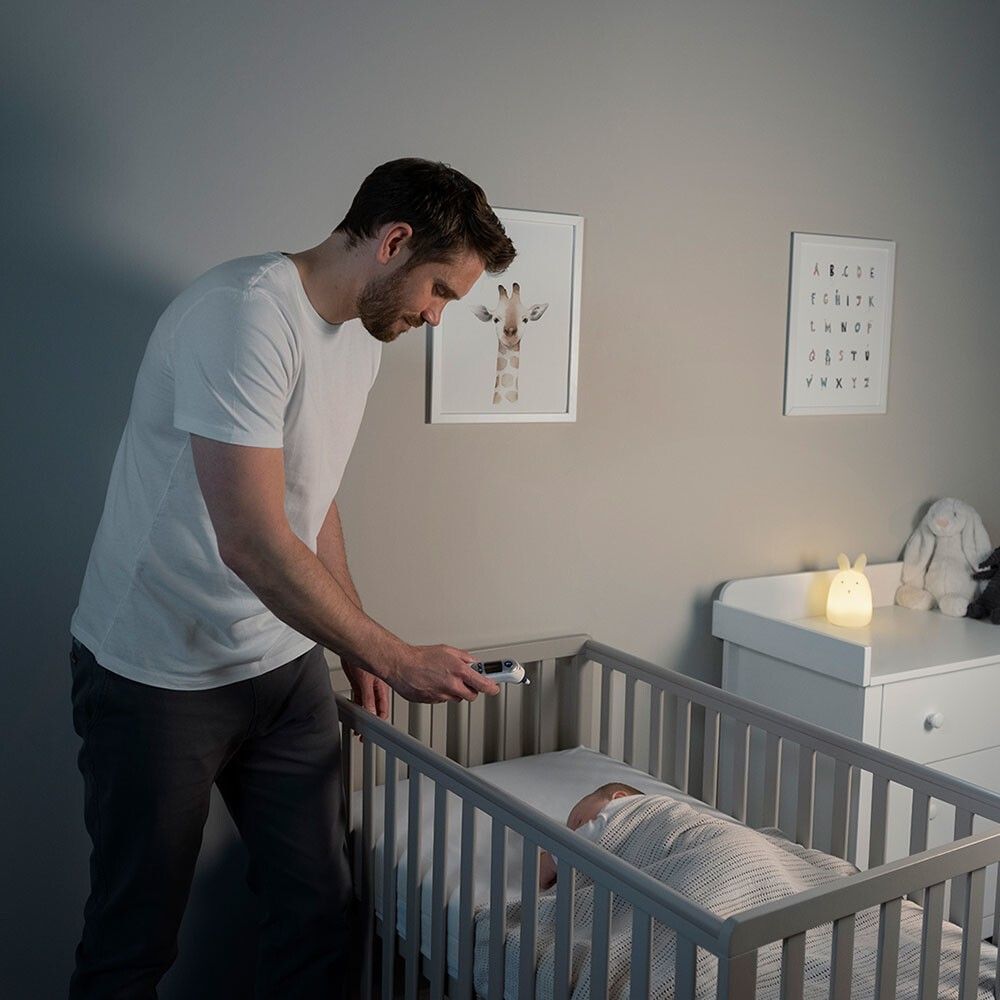 Un uomo misura la temperatura di un bambino a letto con un termometro auricolare. Ambiente scuro.