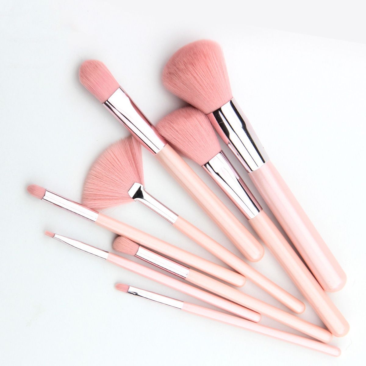 Un set di otto pennelli per il trucco rosa, disposti su sfondo bianco.