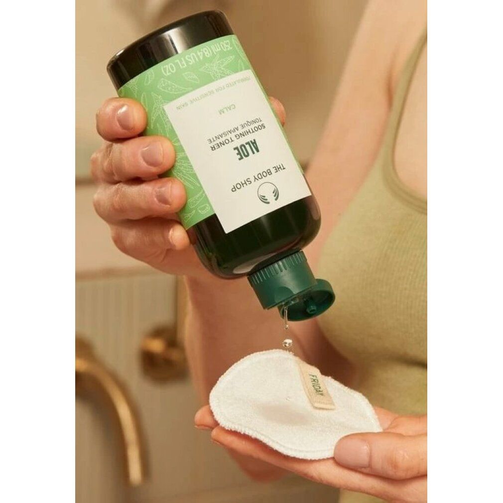 Persona tiene bottiglia verde e versa liquido su dischetto di cotone. Etichetta prodotto visibile. Marchio: The Body Shop.