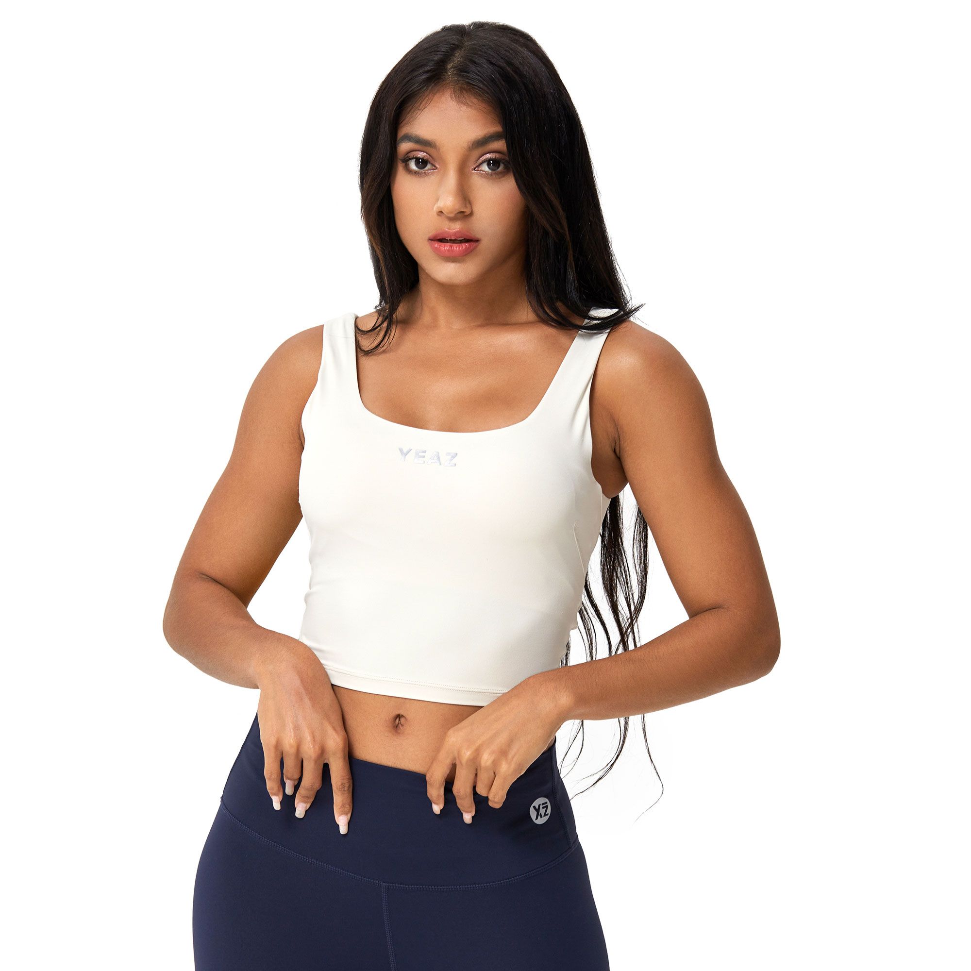 Donna con crop top smanicato color crema a scollo quadrato e leggings blu scuro. Logo discreto sul davanti del top e sulla gamba.