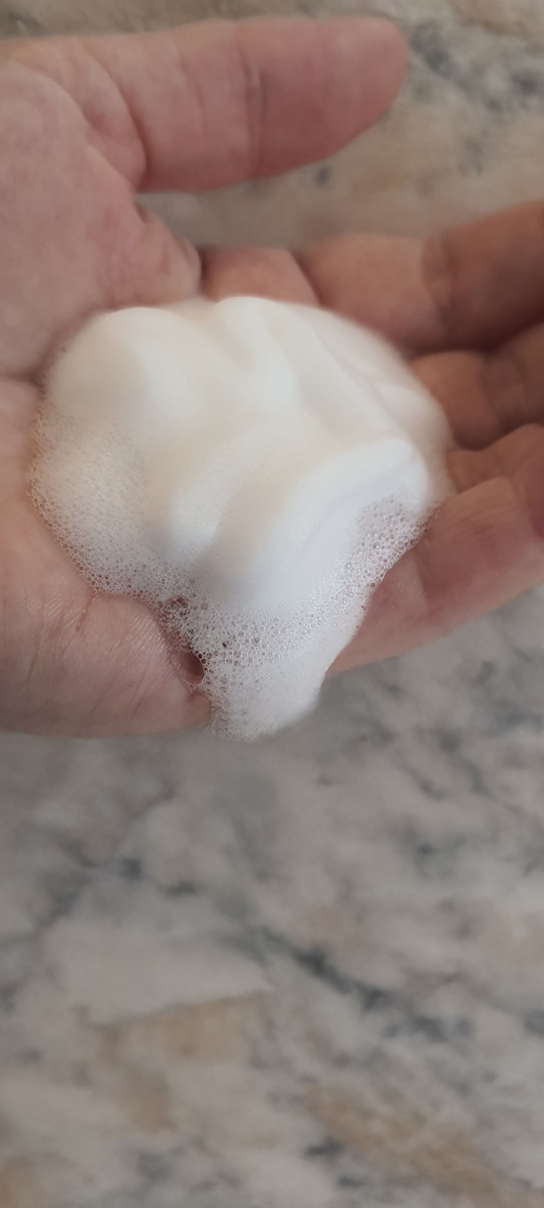 Palmo della mano con schiuma bianca e cremosa. Sfondo: superficie chiara.