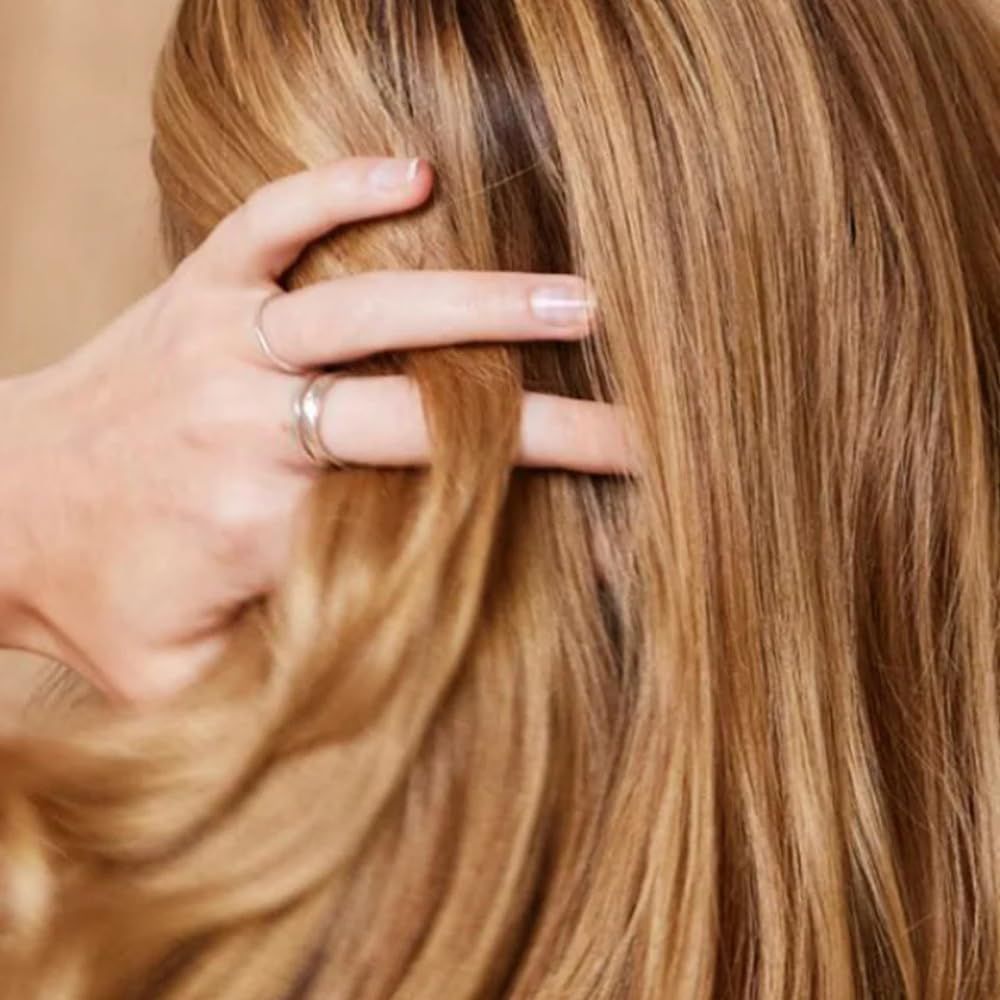 Ciocche di capelli biondi chiari tenute da una mano. La mano indossa anelli. I capelli sono lisci e lucenti.