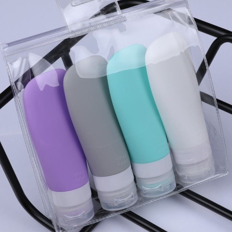Quattro flaconi da viaggio in silicone viola, grigio, turchese e bianco in una busta trasparente.