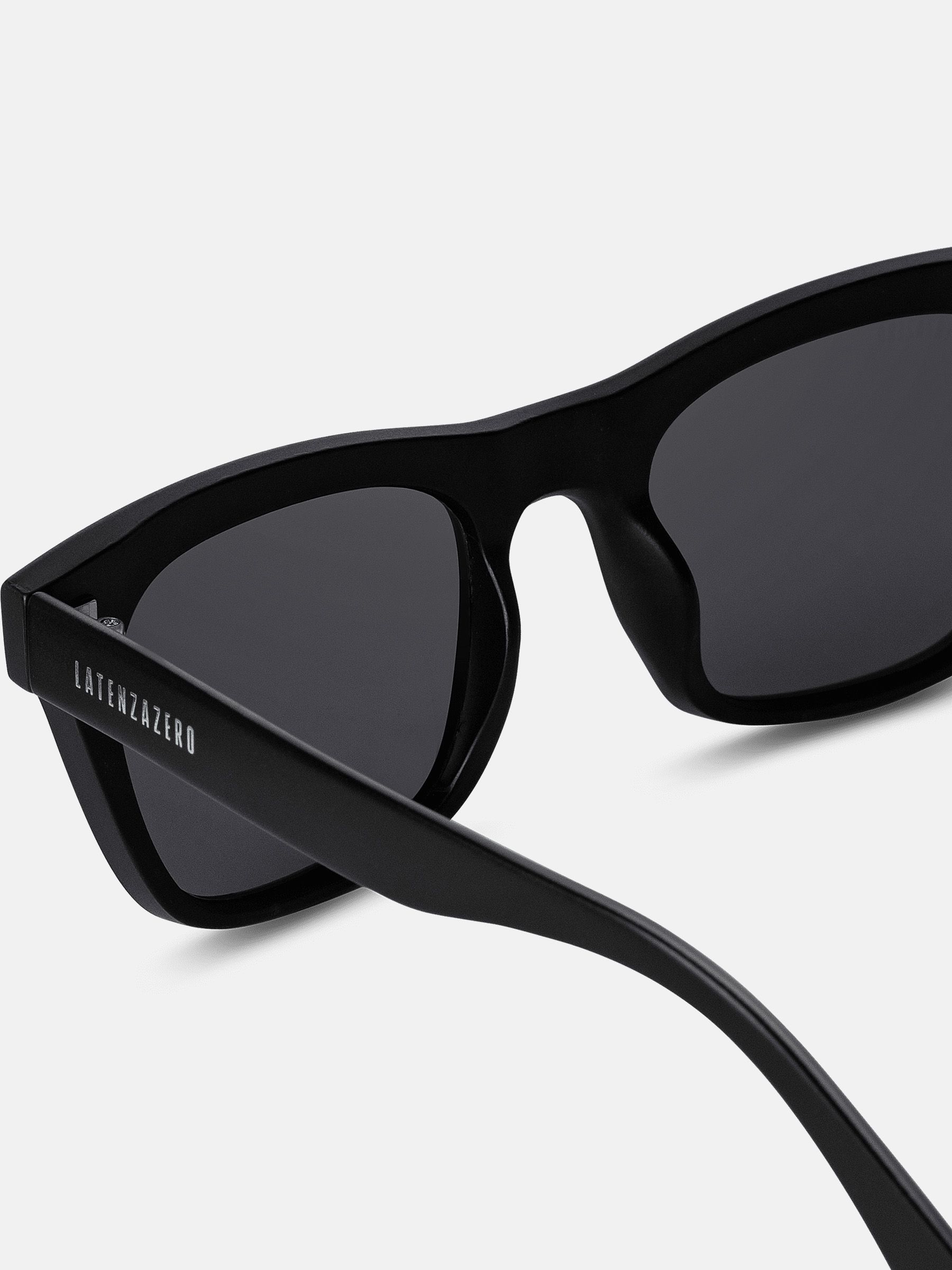 Primo piano di occhiali da sole neri. "LATENZAZERO" sull'asta. Lenti quadrate. Montatura nera.