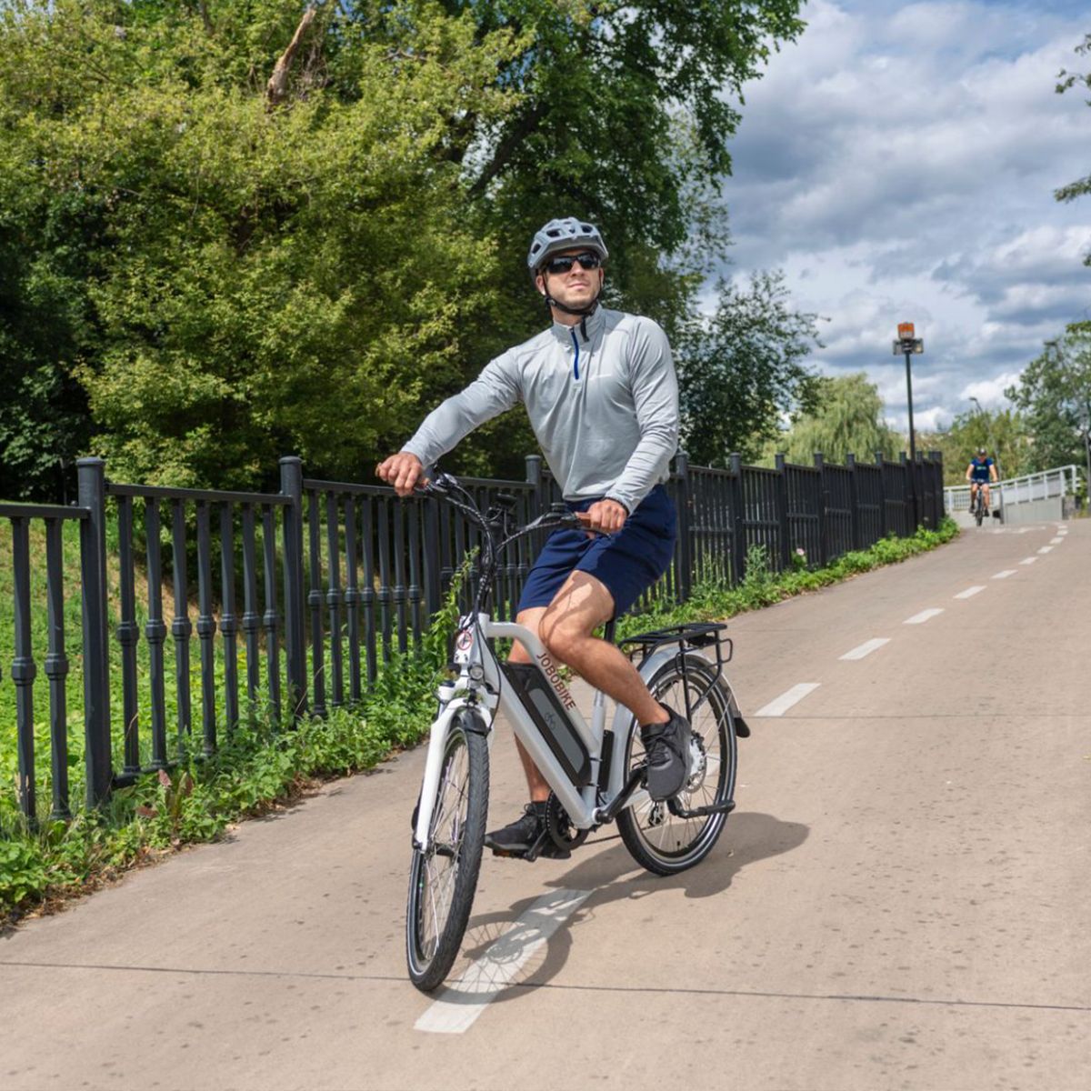 E-bike bianca su pista ciclabile. Ciclista con casco. Logo JOBOBIKE non visibile.