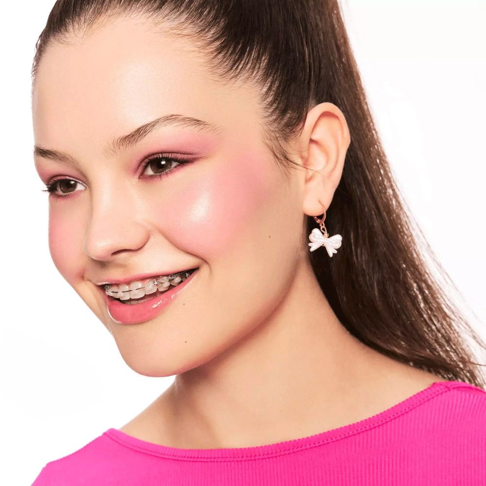 Ritratto di una donna sorridente con guance rosa. Indossa una camicetta rosa e orecchini a forma di fiocco.