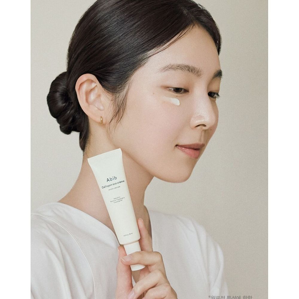 Donna tiene tubo di crema occhi ABIB Collagen. Crema applicata. Prodotto bianco, tubo chiaro con testo nero.