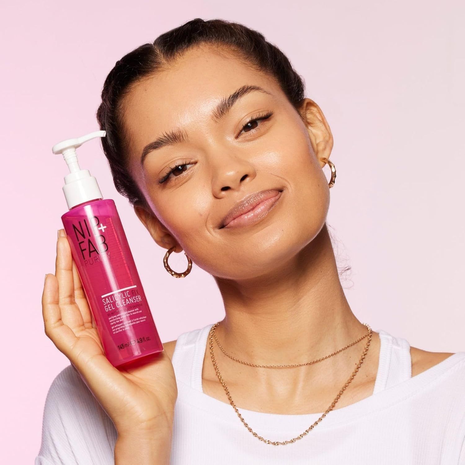 Donna tiene in mano una bottiglia rosa. La bottiglia riporta NIP+FAB e Salicylic Fix Gel Cleanser.