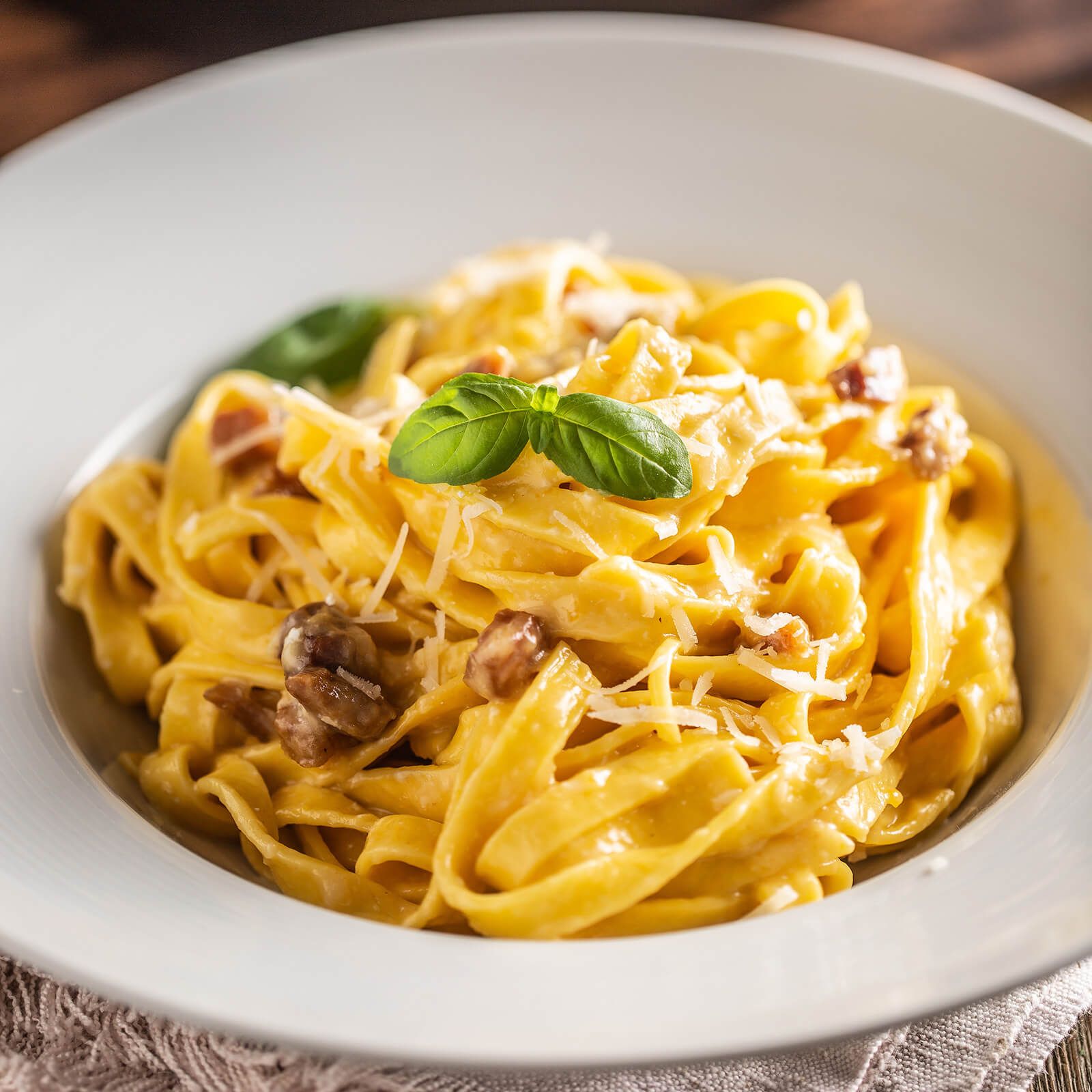 Tagliatelle in una ciotola bianca, ricoperte di salsa, formaggio e foglia di basilico.