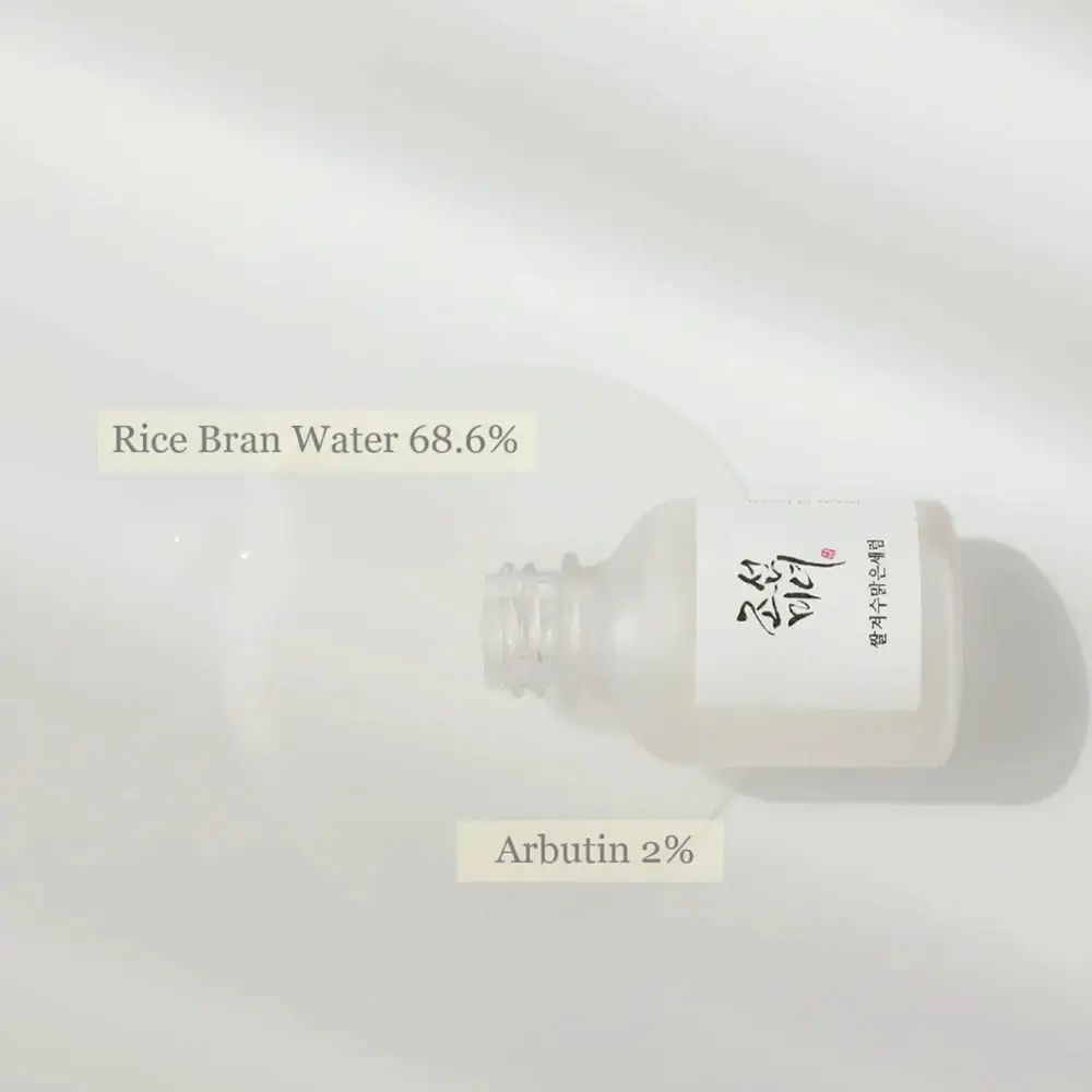 Flacone di vetro con siero. Testo: Rice Bran Water 68,6%, Arbutin 2%.