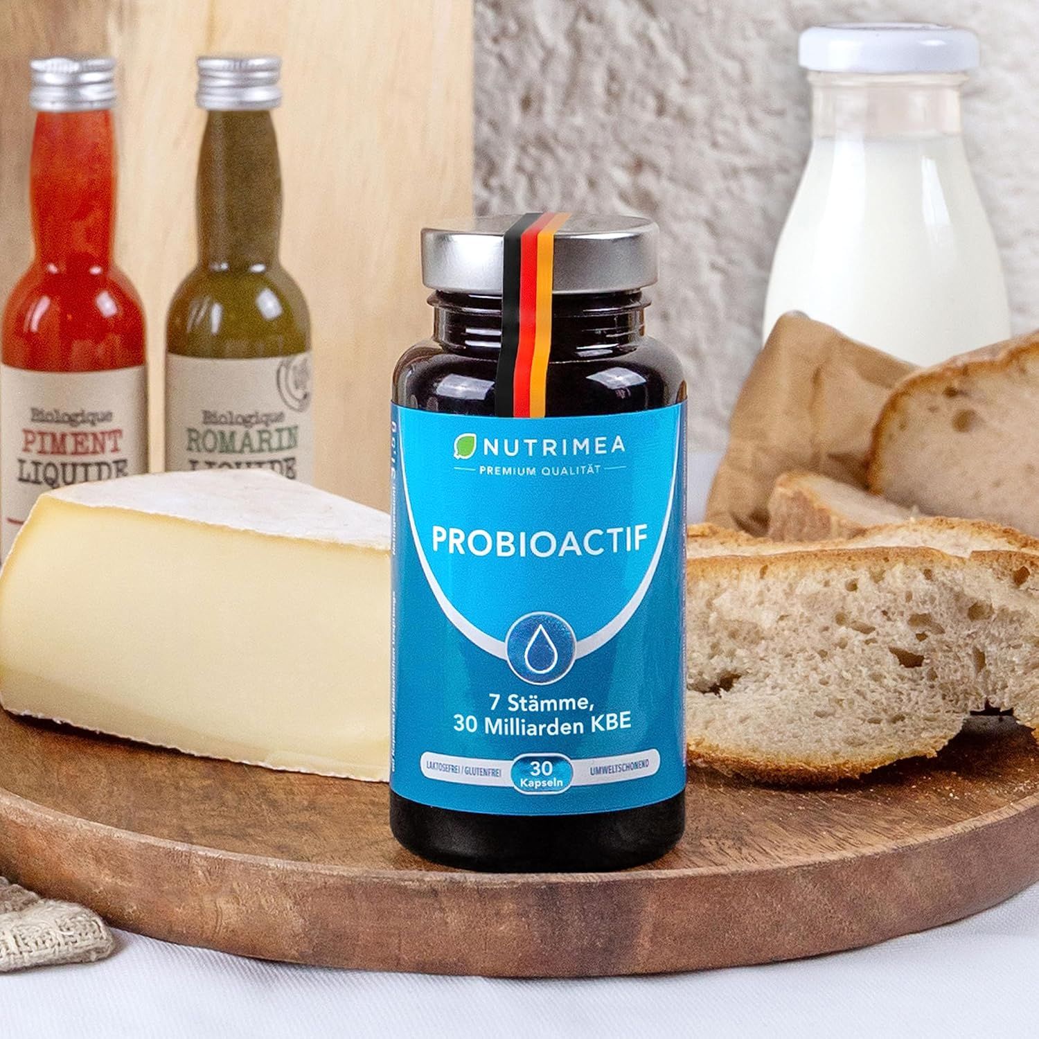 Flacone PROBIOACTIF su tagliere in legno. Pane, formaggio, salse sullo sfondo. Bandiera tedesca sul flacone.