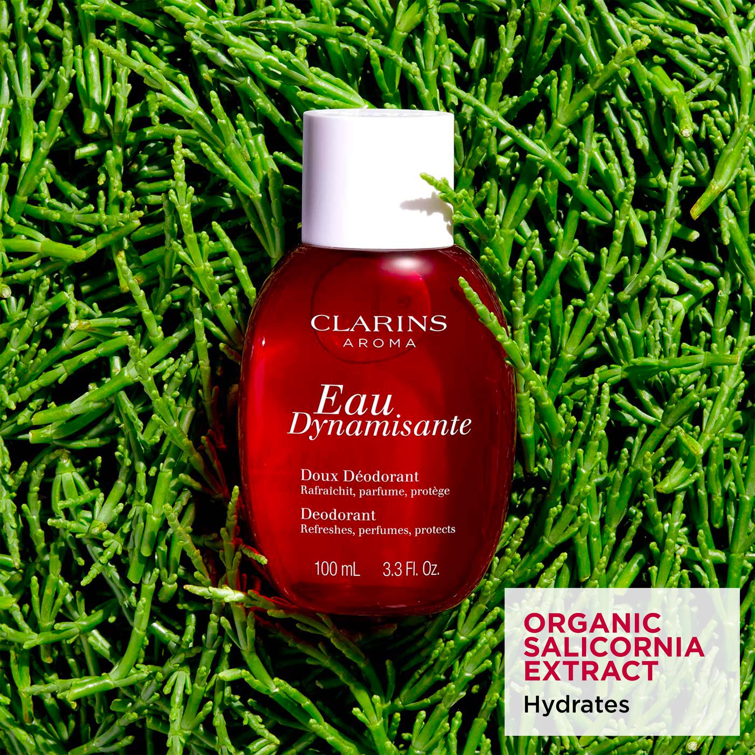 Flacone rosso con tappo bianco. Testo: Clarins Aroma, Eau Dynamisante, Doux Déodorant, Deodorant. Su sfondo verde.