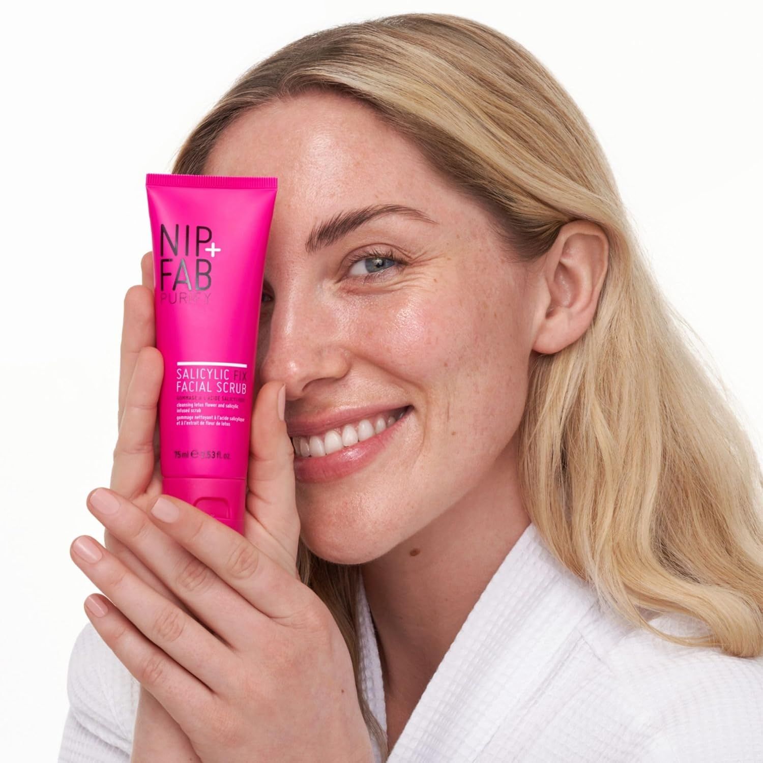 Donna tiene un tubo rosa davanti al viso. Il tubo reca la scritta "NIP+FAB" e "Salicylic Facial Scrub".