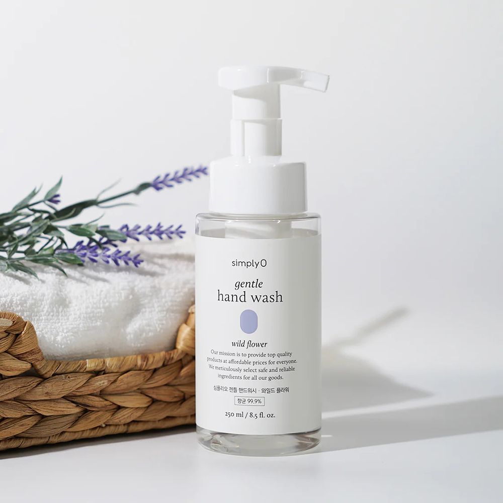 Flacone trasparente con dosatore bianco. Etichetta con nome del prodotto e motivo floreale. Su cesto con asciugamano e lavanda.