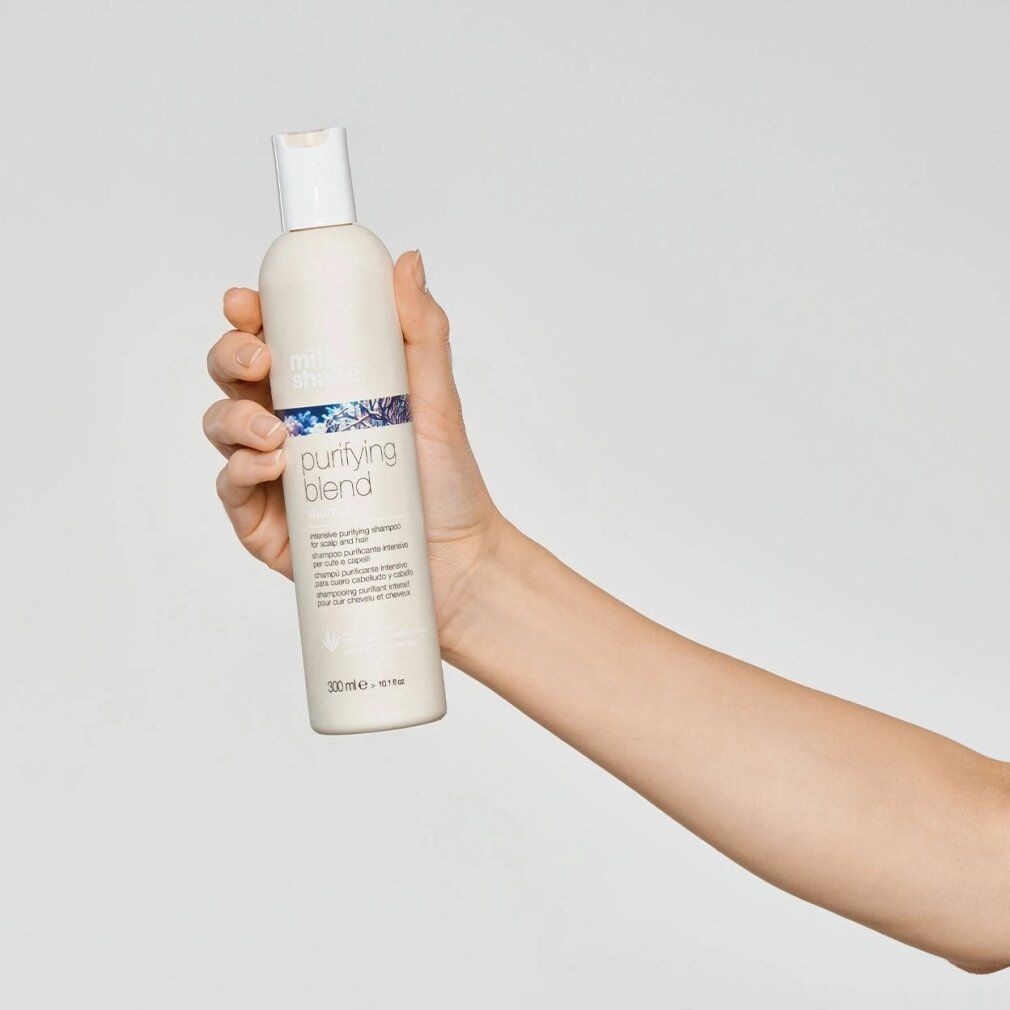 Mano che tiene un flacone di shampoo beige con tappo bianco. Scritta: purifying blend. Testo sottostante: intensive purifying shampoo. In basso: 300 ml.