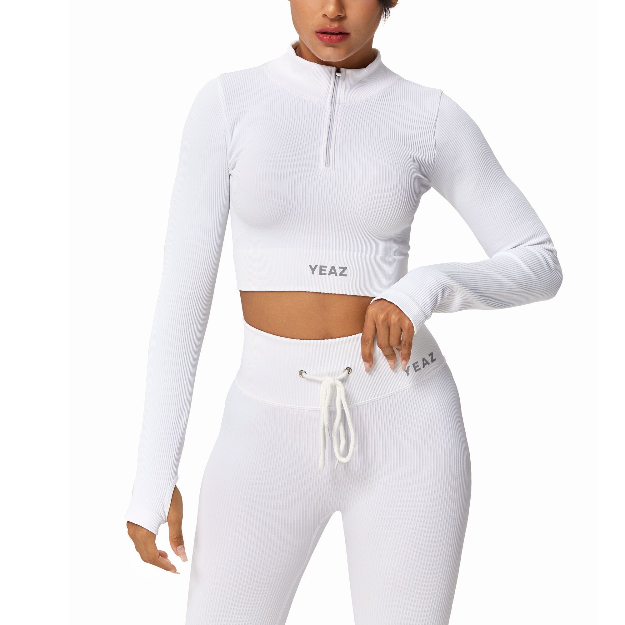 Crop top bianco a costine a maniche lunghe con zip e fori per i pollici. Marchio 'YEAZ' sul top e sui pantaloni.