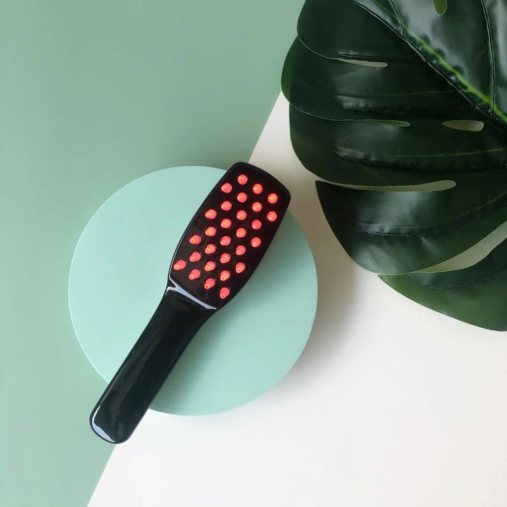 Spazzola per capelli nera con molti LED rossi, appoggiata su un cerchio verde menta.