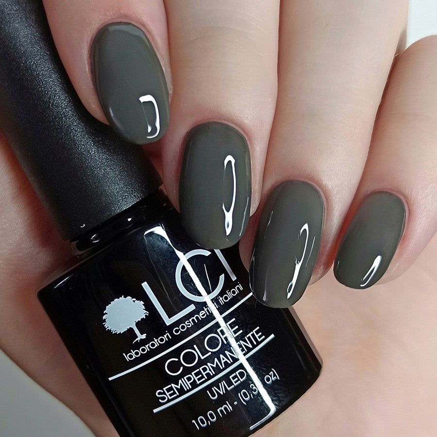 Mano con unghie smaltate grigie. Flacone di smalto con scritta: LCI, Colore Semipermanente, UV/LED 10,0 ml.