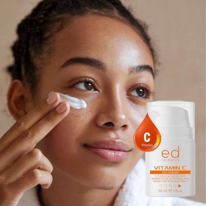 Donna che applica la crema per gli occhi. Flacone di crema per occhi bianco con etichetta arancione. Testo: Vitamin C Eye Cream, 30 ml, 1 fl.oz. Marchio: ed cosmetics.