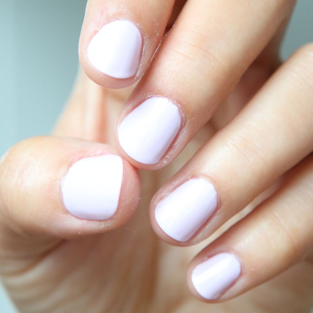 Primo piano di cinque dita con smalto lilla chiaro. Le unghie sono corte e smaltate.