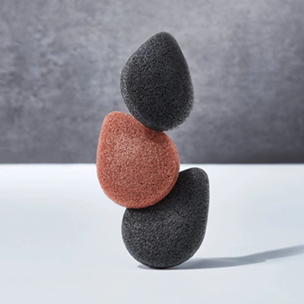 Tre spugne Konjac in equilibrio. Due nere, una rosso-marrone. Forma a goccia.