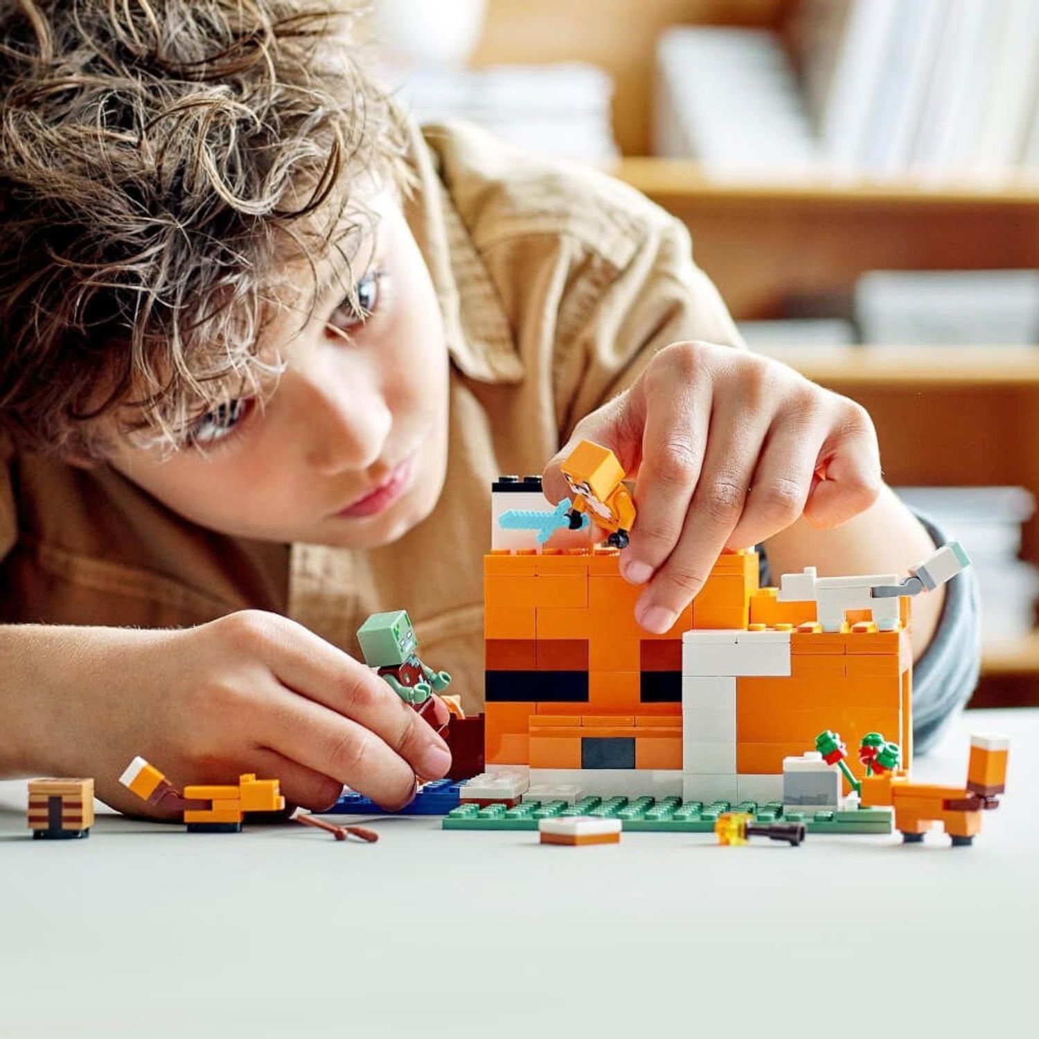 Bambino che costruisce LEGO Minecraft 21178. Edificio arancione e bianco. Personaggi: volpe, zombie, volpi. Bambino in primo piano.