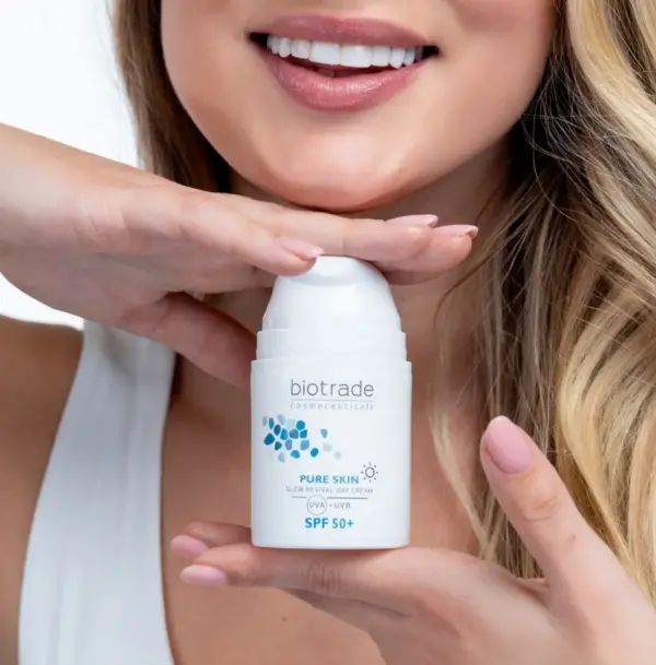 Donna che tiene in mano un flacone di crema bianco. Scritta: Biotrade, Pure Skin, SPF 50+. La donna sorride.