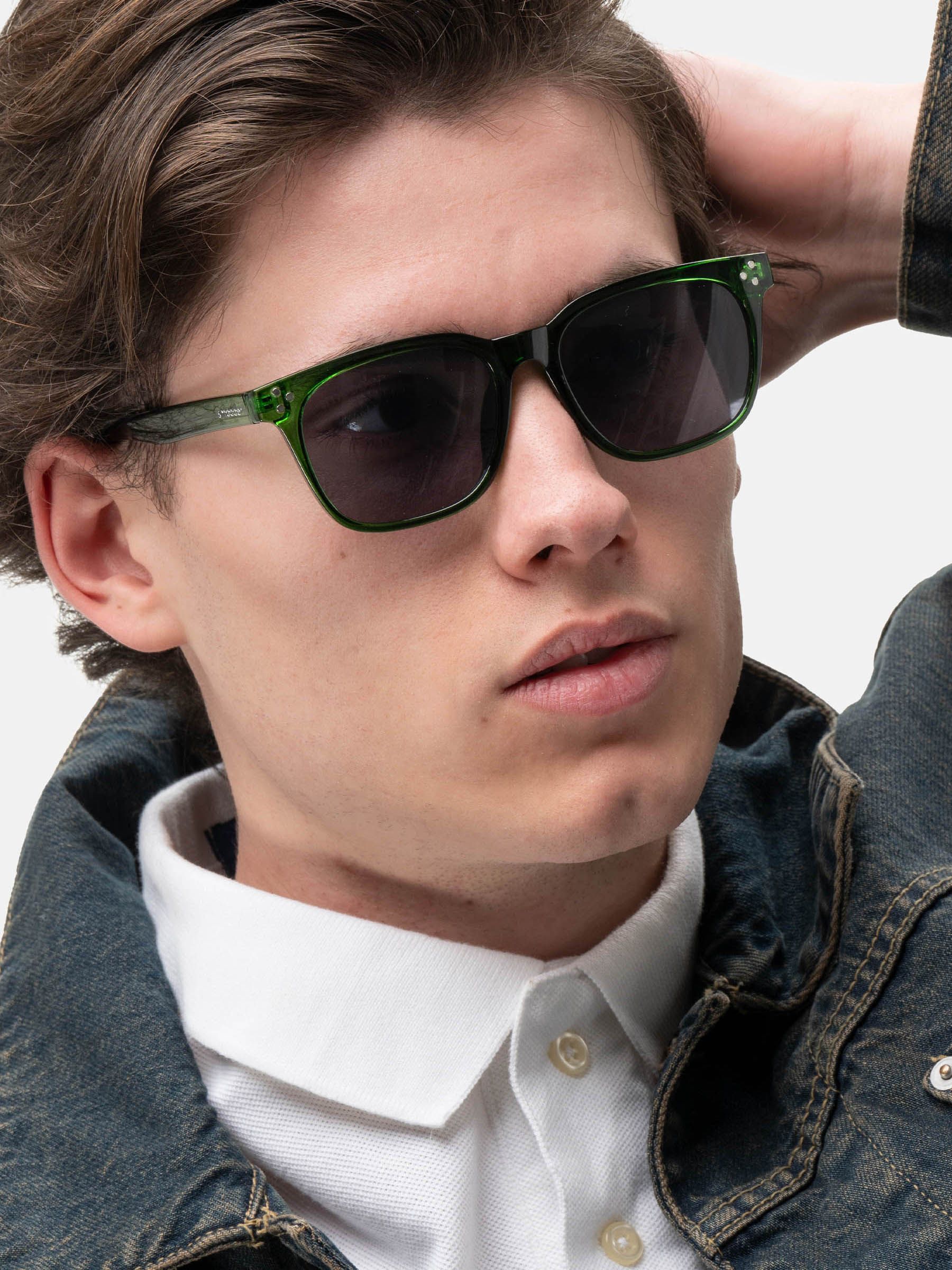 Uomo con occhiali da sole verdi. Forma quadrata, lenti scure. Indossa giacca di jeans e camicia bianca.