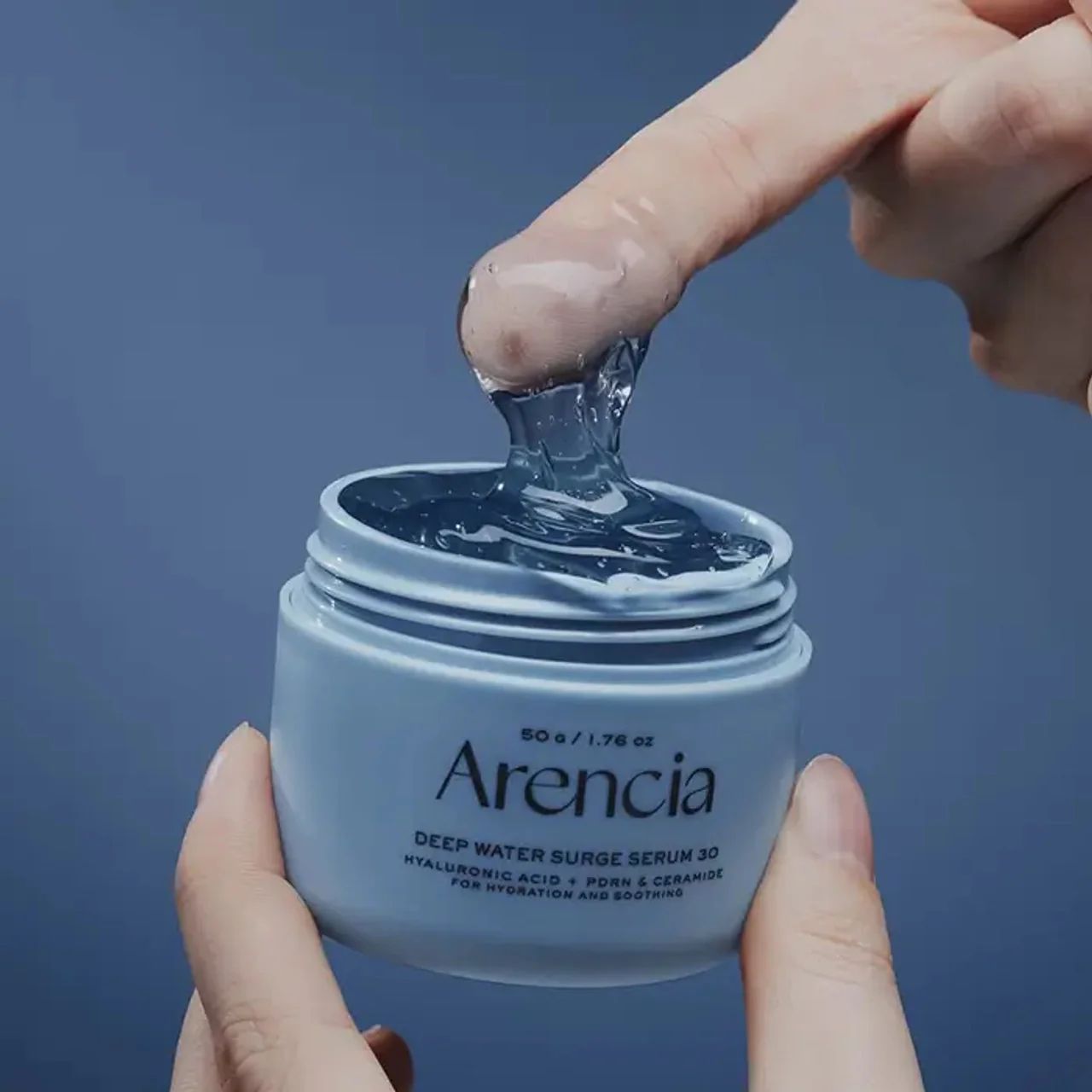 Vasetto azzurro con AENCIA DEEP WATER SURGE SERUM 30. Texture gel trasparente prelevata con il dito.