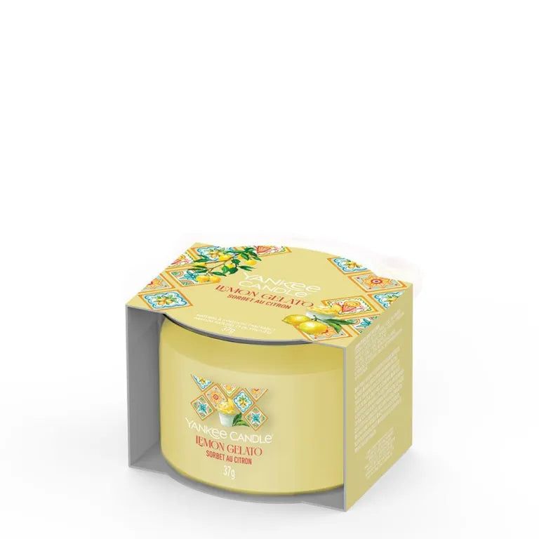 Candela gialla nella confezione. Scritta: Lemon Gelato. Confezione con motivi floreali. Candela cilindrica.