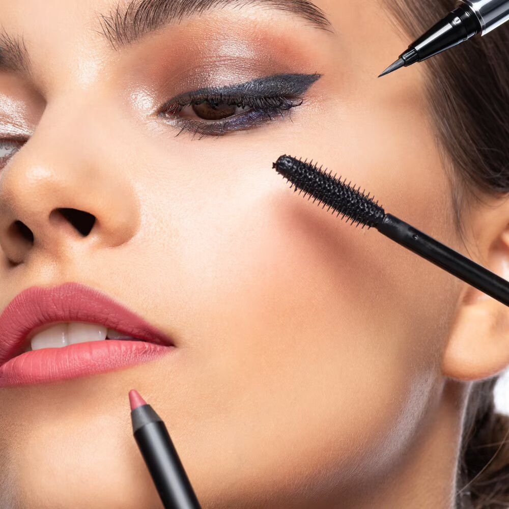 Viso di donna truccata. Visibili mascara, eyeliner e rossetto. Spazzola per mascara vicino all'occhio.